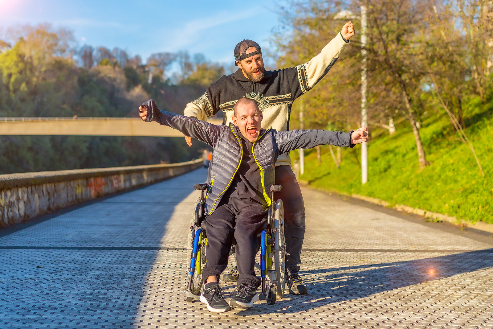 Disabled Person In Wheelchair With Friend Overjoyed, Smiling, En