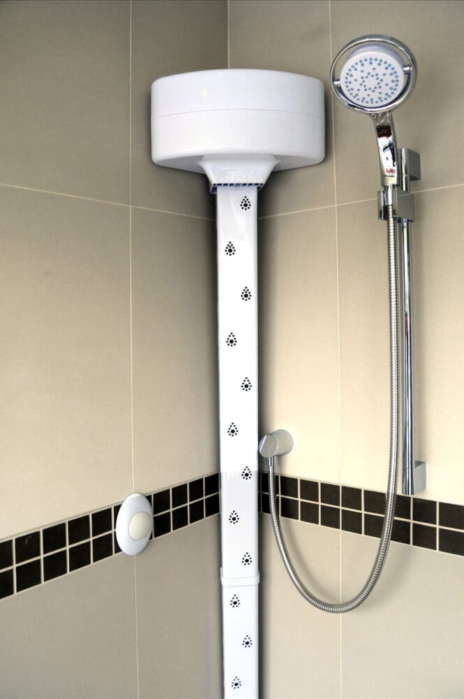 A bathroom body dryer placed next to a shower head on cream tiles.
