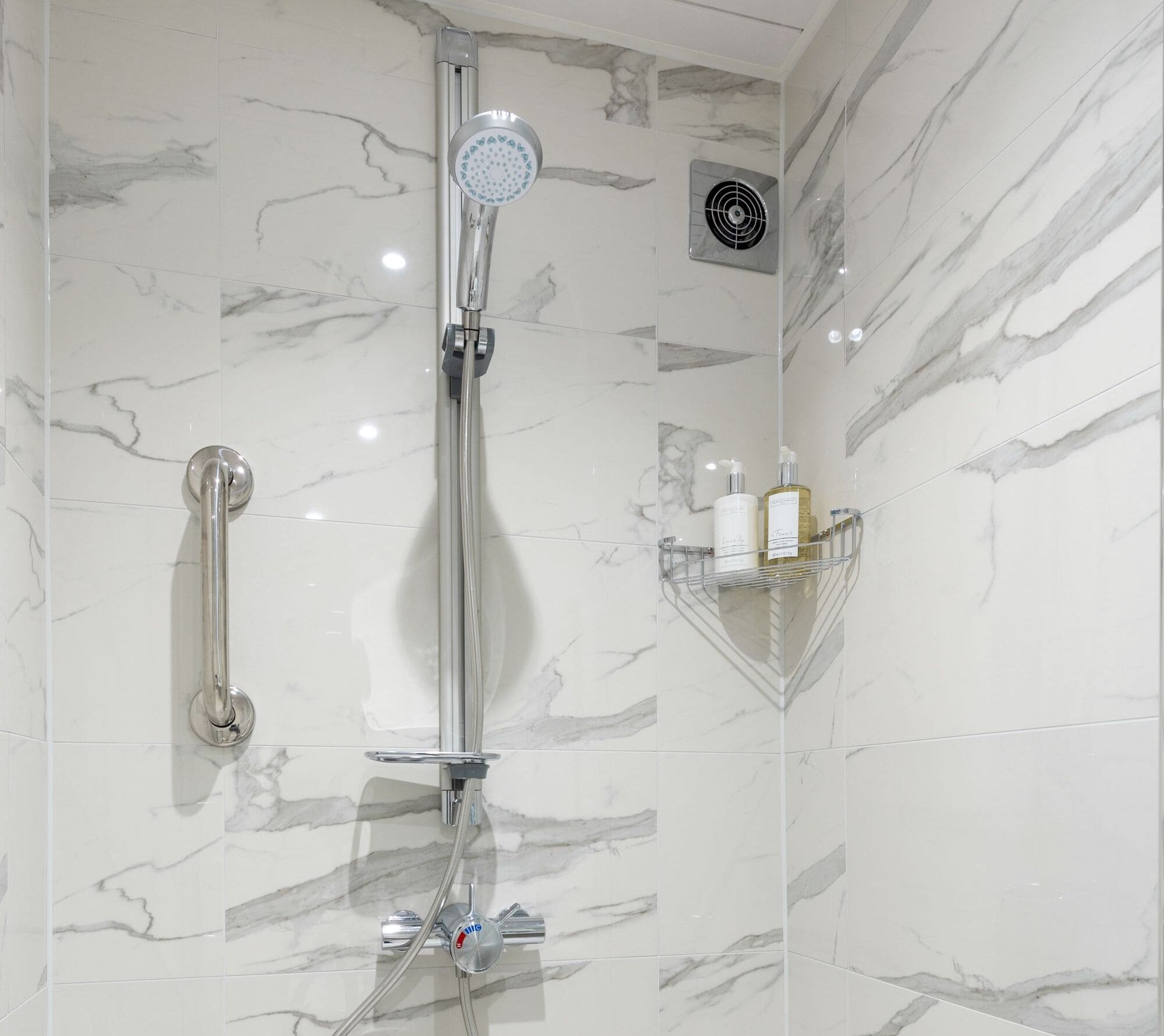 A vertical grabrail placed on the wall next to a shower with marbled wall panelling.