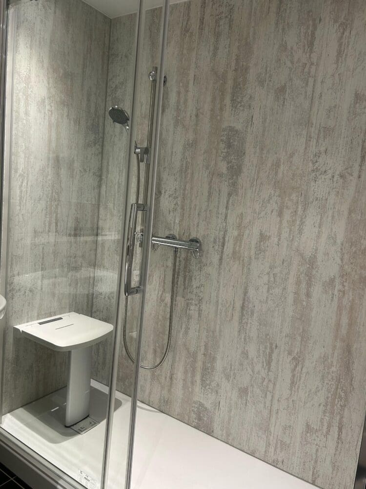 This image shows a Shower Area with a wall fixed white Seat and glass shower enclosure